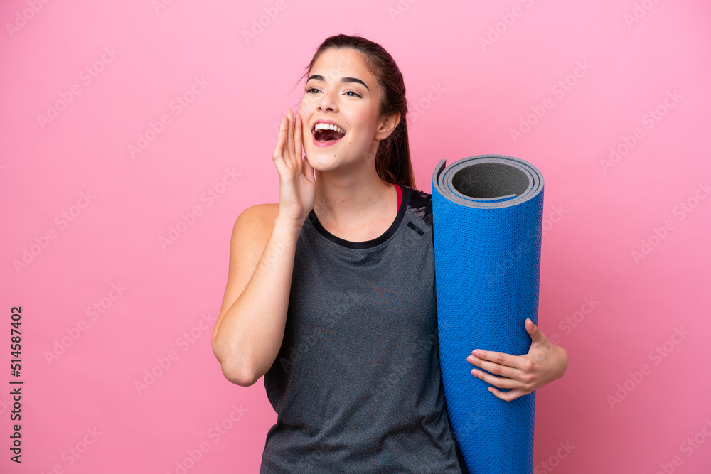 Young Brazilian sport woman going to yoga classes while holding a mat isolated on pink background shouting with mouth wide open to the side Young Brazilian sport woman going to yoga classes while holding a mat isolated on pink background shouting with mouth wide open to the side