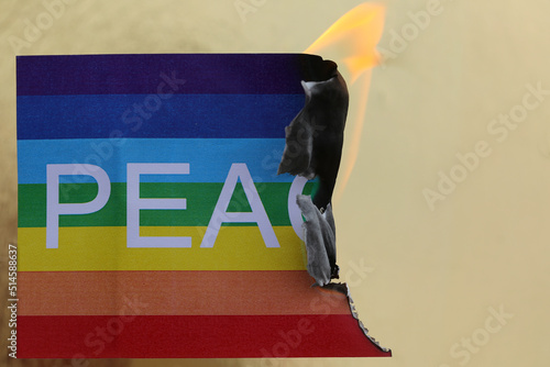 multicolored peace flag as it burns and the flame erasing some of the text