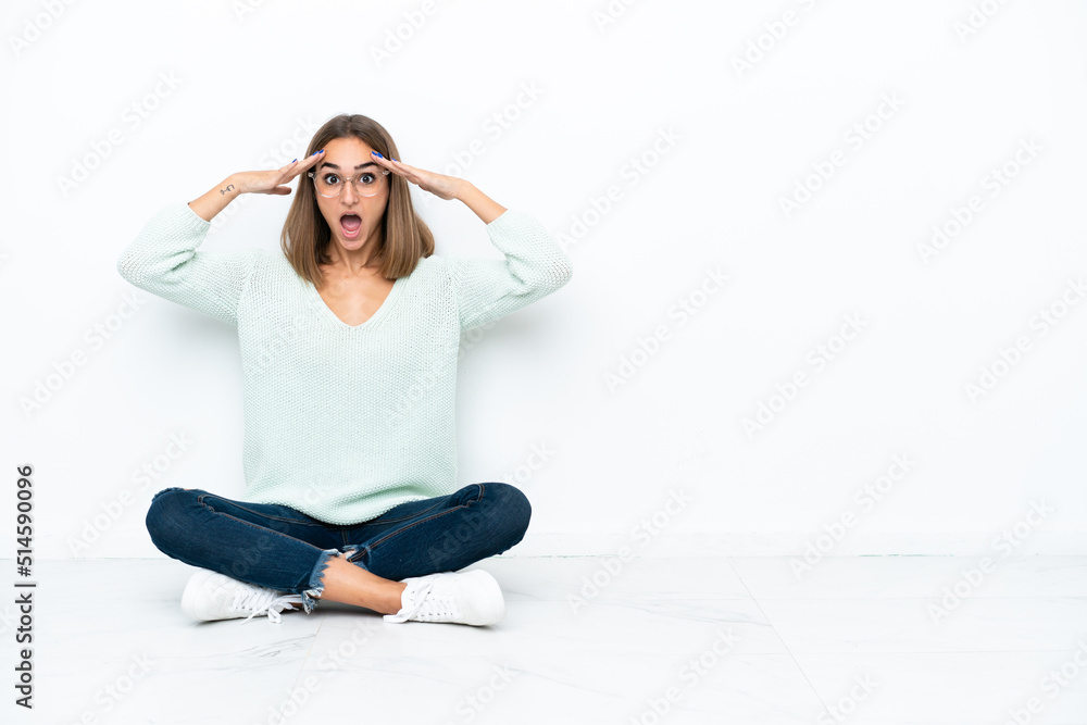 Fototapeta premium Young caucasian woman sitting on the floor isolated on white background with surprise expression
