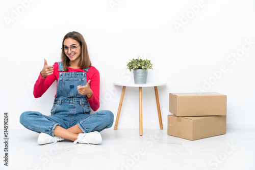 Young caucasian woman sitting on the floor among boxes pointing to the front and smiling