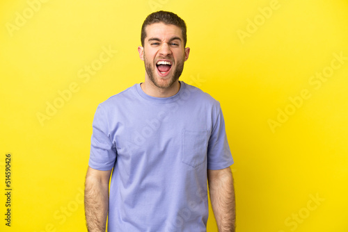 Handsome blonde man over isolated yellow background shouting to the front with mouth wide open