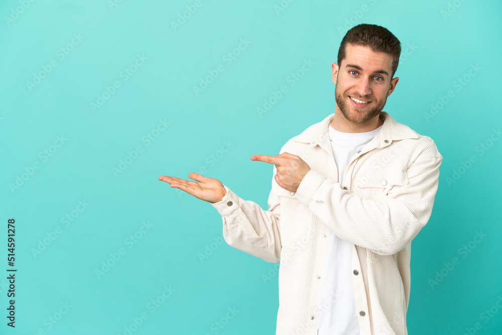 Handsome blonde man over isolated blue background holding copyspace imaginary on the palm to insert an ad Handsome blonde man over isolated blue background holding copyspace imaginary on the palm to insert an ad