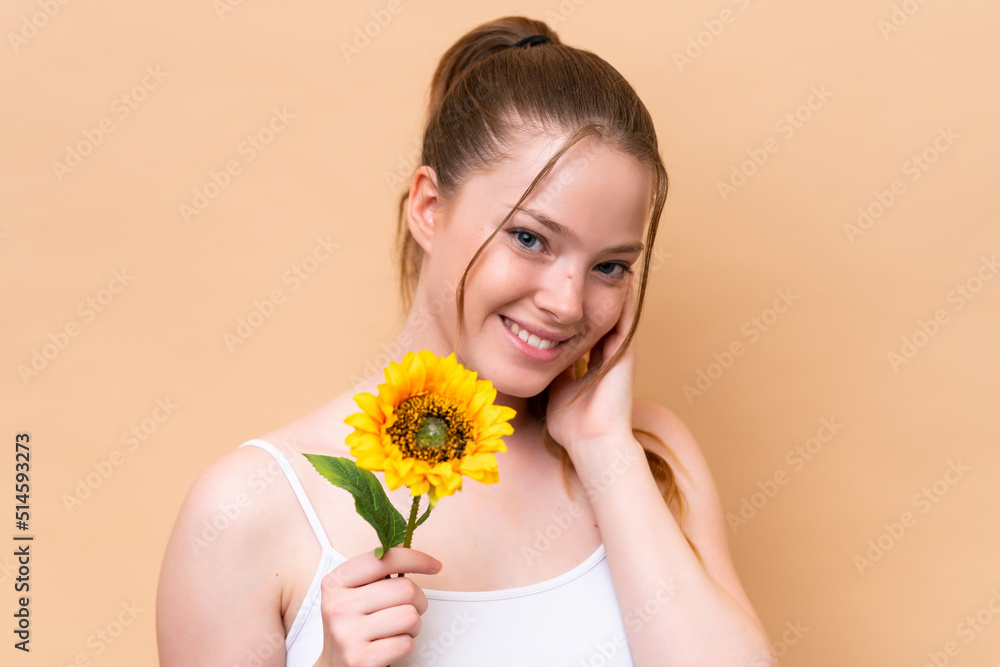 Young caucasian girl isolated on beige background holding a sunflower while smiling. Close up portrait Young caucasian girl isolated on beige background holding a sunflower while smiling. Close up portrait