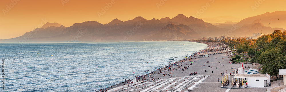 Fototapeta premium Sunset panoramic view of scenic and popular Konyaalti beach in Antalya resort town. Majestic mountains with haze in the background. Vacation and holiday in Turkey