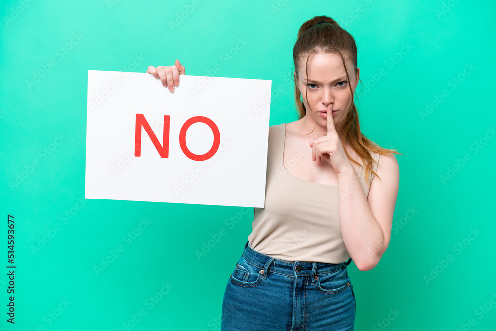Young caucasian woman isolated on green background holding a placard with text NO doing silence gesture Young caucasian woman isolated on green background holding a placard with text NO doing silence gesture