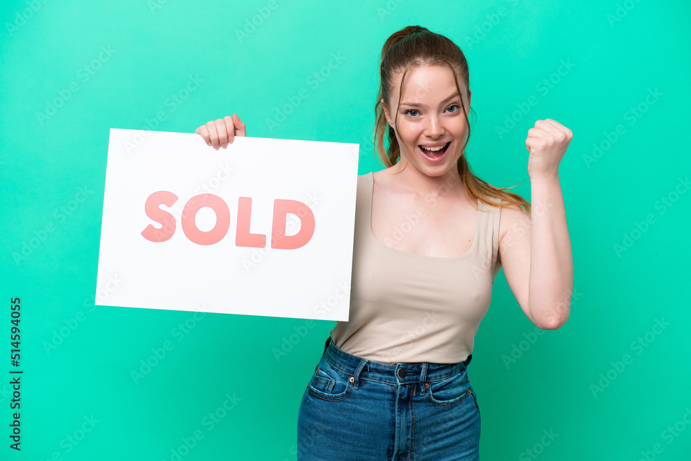 Young caucasian woman isolated on green background holding a placard with text SOLD and celebrating a victory Young caucasian woman isolated on green background holding a placard with text SOLD and celebrating a victory
