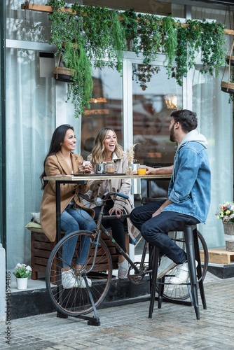 Group of cool friends sharing a brunch together while talking and looking the smartphone on the healthy coffee shop terrace.