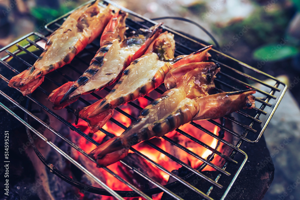 Large prawns are placed on an iron griddle and grilled over a hot coal