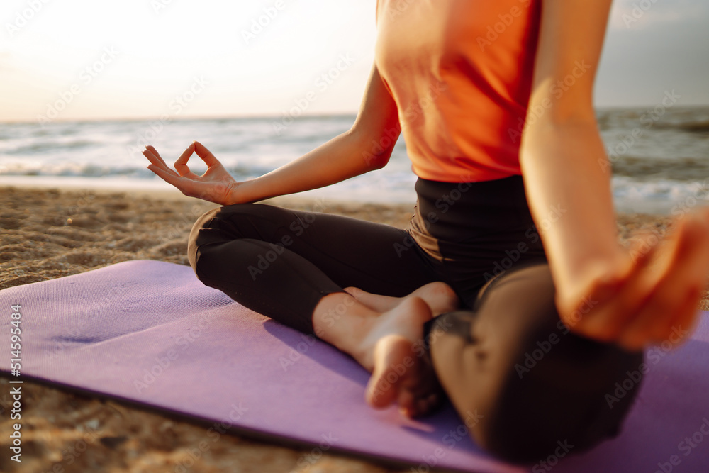 Beautiful woman doing yoga near the ocean barefoot. Young woman in sportswear doing fitness exercise on the beach. Calmness and balance, a healthy lifestyle.