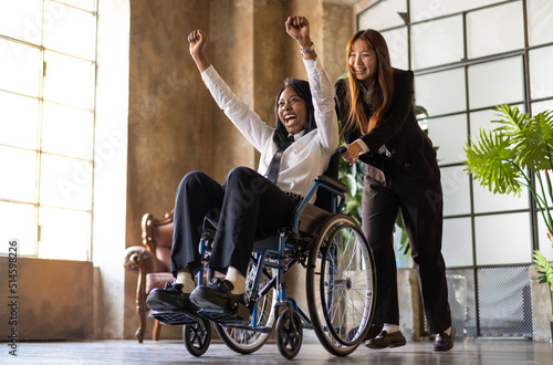Young asian woman pushing  african american collegue in wheelchair in co-working studio-  Good vibes, social inclusion and positivity moments in the workplace photo
