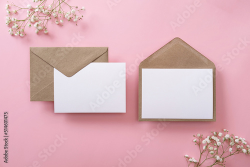 Blank greeting cards and envelopes with gypsophila on pink background. Blank paper sheet cards with mockup copy space. Minimal workplace composition. Flat lay, top view