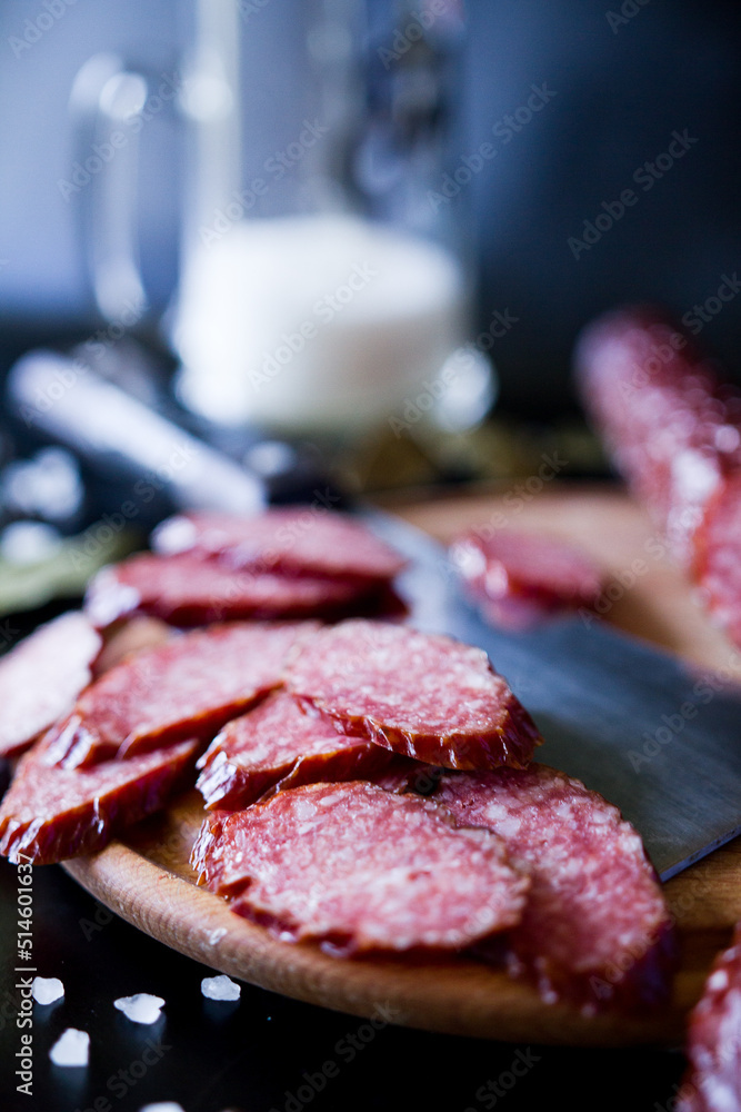 Salami and beer. Salami is cut into slices with a large knife. Smoked sausage. Salami sausage on a wooden board ona a black background. sausage with spices. A glass of beer with a sausage. Salami and beer. Salami is cut into slices with a large knife. Smoked sausage. Salami sausage on a wooden board ona a black background. sausage with spices. A glass of beer with a sausage.