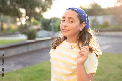 Portrait of cute happy teenage girl with long hair, wearing a blue bandana, yellow t-shirt. Caucasian. The concept of natural beauty, happiness, young skin, childhood. Summer time. Sunset. Soft focus. © Larysa