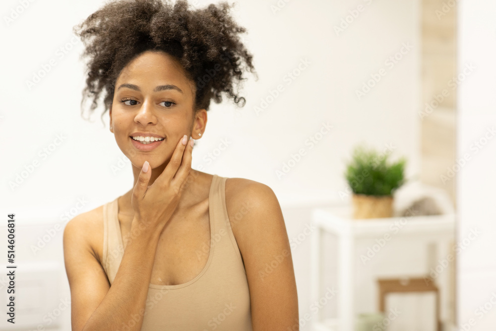 Happy woman admiring her skin in front of a bathroom mirror, touching her face with her hand Happy woman admiring her skin in front of a bathroom mirror, touching her face with her hand