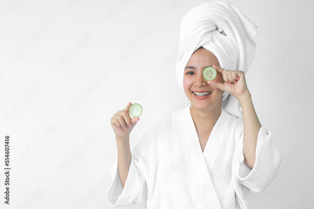 Young beautiful asian girl caucasian smiling hiding eye behind cucumber slice over white background. Beauty spa skin care therapy and cosmetology concept. Young beautiful asian girl caucasian smiling hiding eye behind cucumber slice over white background. Beauty spa skin care therapy and cosmetology concept.