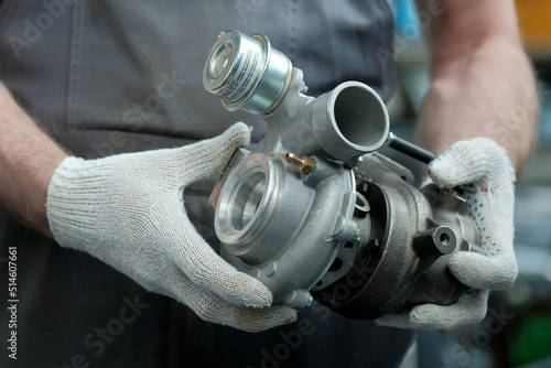 Car maintenance. An auto mechanic holds a new turbocharger in his hands. Inspection and control of the spare part for the engine for compliance and integrity. photo