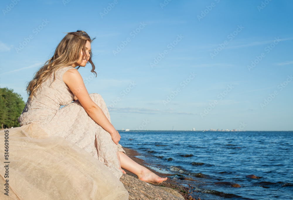 Young cute barefoot girl model in a beige dress on the beach