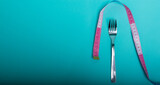 Healthy eating, weight loss obesity. Fork cutlery with a measuring tape in centimeters on a blue background from above. Diet menu.Place for an inscription. Advertising.