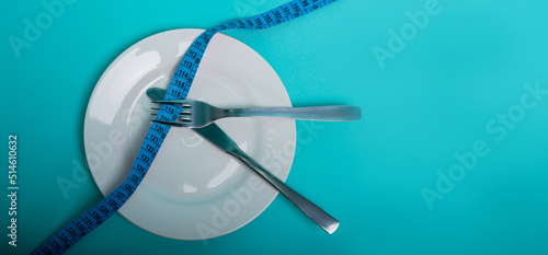 Healthy eating, weight loss obesity. An empty plate with a measuring tape in centimeters, a fork and a knife on a blue background from above. Diet menu.Place for an inscription. Advertising.