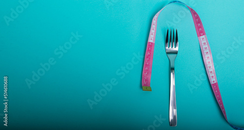 Healthy eating, weight loss obesity. Fork cutlery with a measuring tape in centimeters on a blue background from above. Diet menu.Place for an inscription. Advertising.