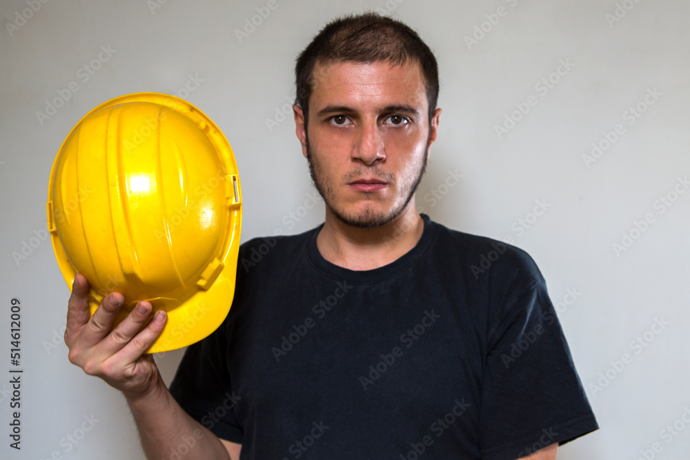 Worker with yellow safety hat for construction site work. Young white caucasian man with short hair and dark eyes. Worker with yellow safety hat for construction site work. Young white caucasian man with short hair and dark eyes.