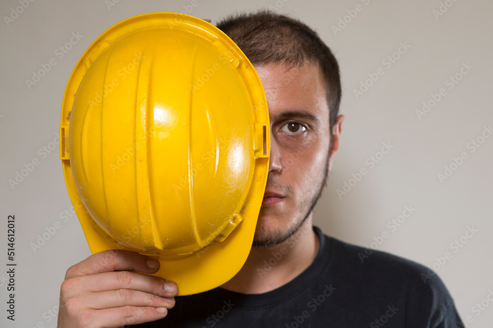 Worker with yellow safety hat for construction site work. Young white caucasian man with short hair and dark eyes. Worker with yellow safety hat for construction site work. Young white caucasian man with short hair and dark eyes.