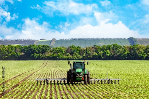 green tractor plowing the soil in a field on a summer sunny day