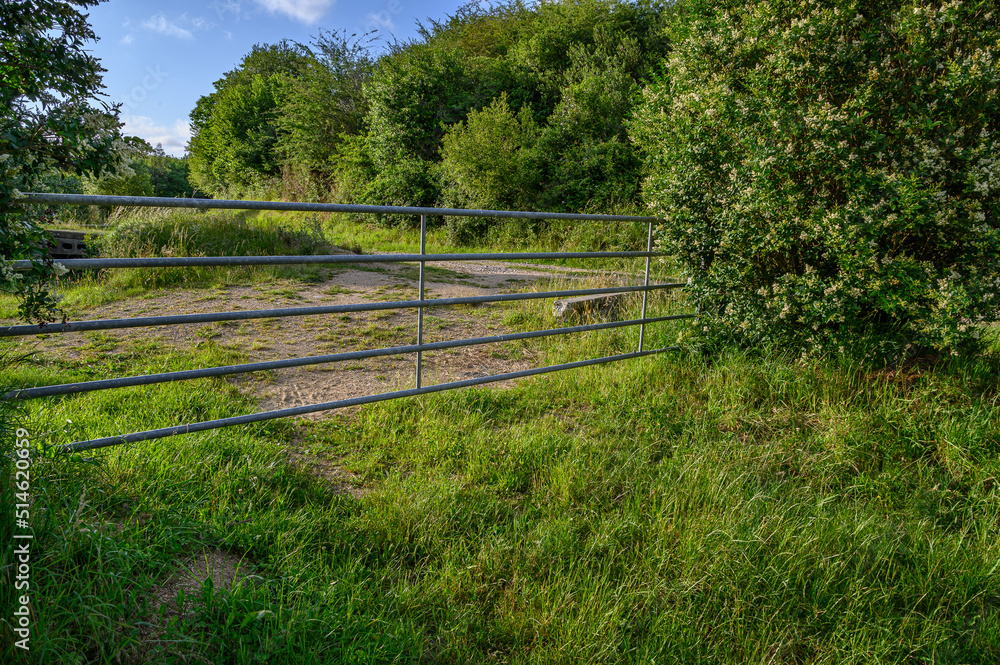 elongated metal fence in the middle of the field, behind it a plowed field prepared for planting, on the sides and in the background bushes and a forest of very leafy and green trees
elongated metal fence in the middle of the field, behind it a plowed field prepared for planting, on the sides and in the background bushes and a forest of very leafy and green trees