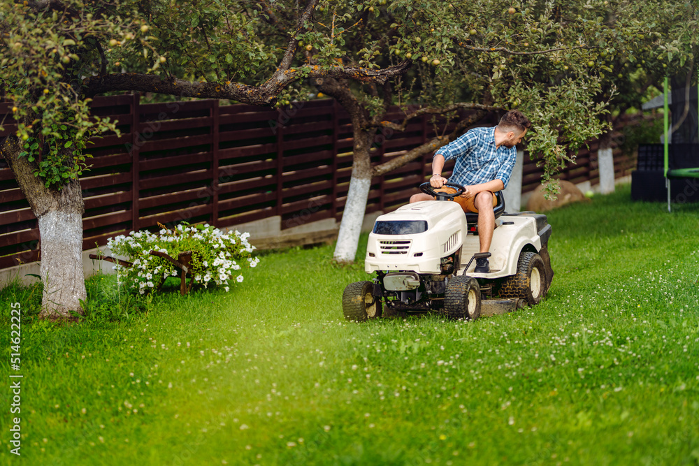 Professional gardener driving a riding lawn mower in a garden. Industrial landscaping works.