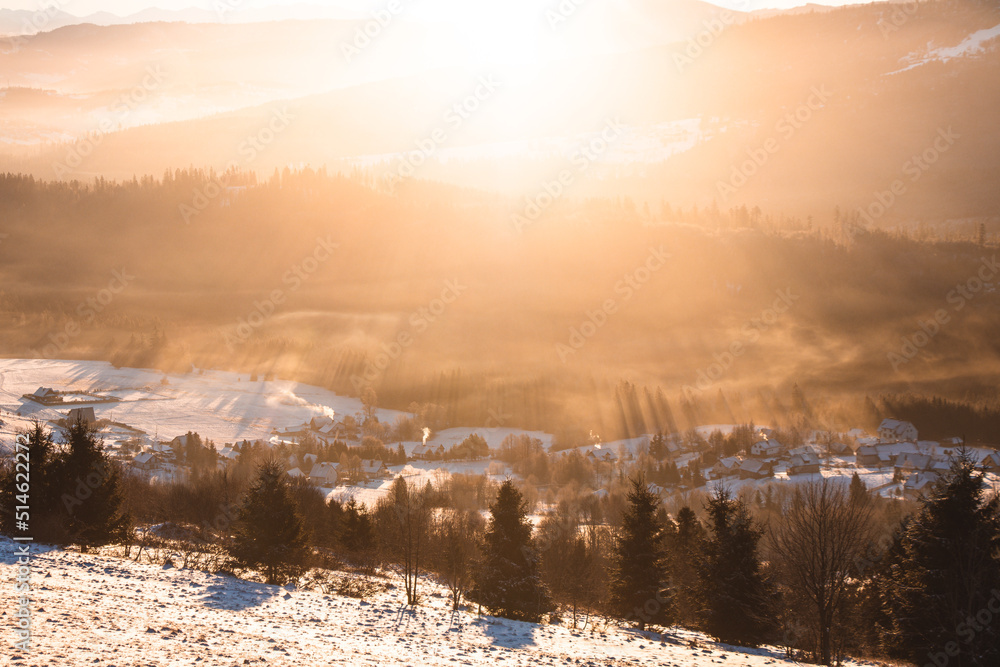 Sunrise over the Polish village of Koniakow with the forest cover through which the sun's rays pass in the morning mist. A breathtaking sight on a cold morning Sunrise over the Polish village of Koniakow with the forest cover through which the sun's rays pass in the morning mist. A breathtaking sight on a cold morning