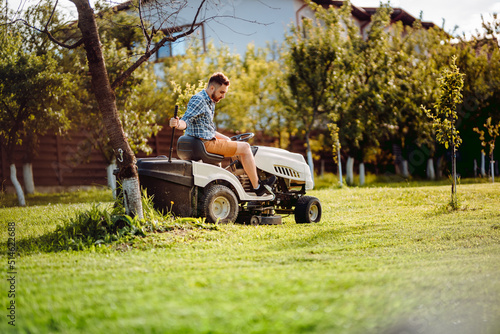 Industry details - portrait of gardener mowing lawn, cutting grass in garden using tractor