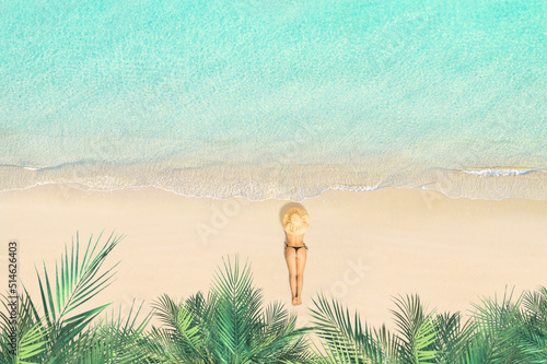 Top view of woman in bikini and straw hat lying and sunbathes on tropical Seychelles sea sand beach with palm tree grove. Aerial, drone view