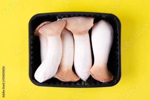 King oyster mushrooms, eringi, in a container on yellow background. Top view photo