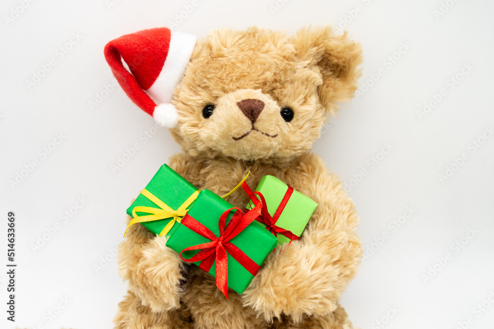 A stuffed toy Teddy bear in a red Santa Claus hat with a pompom on one ear, holding green gift boxes in its paws. White background, copy space. The concept of Christmas gifts, sales A stuffed toy Teddy bear in a red Santa Claus hat with a pompom on one ear, holding green gift boxes in its paws. White background, copy space. The concept of Christmas gifts, sales