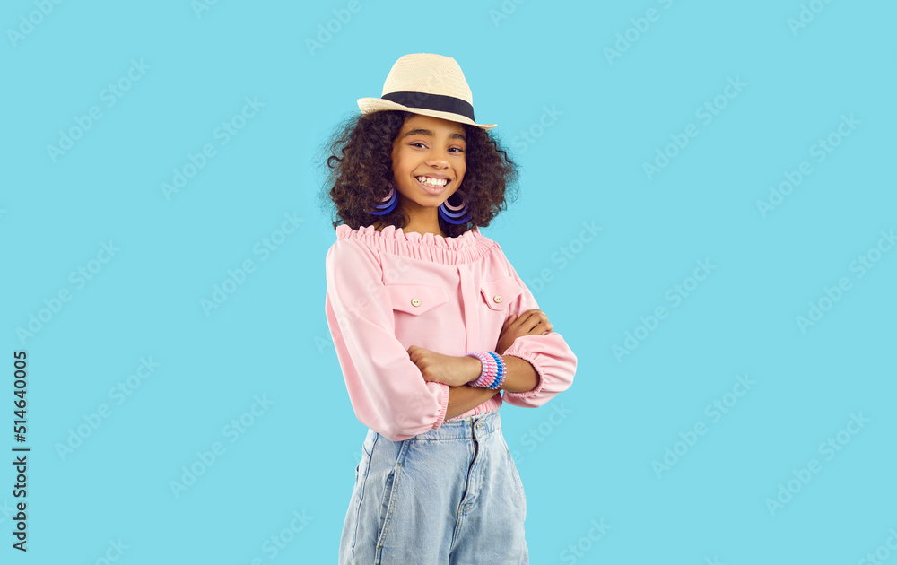Joyful child model posing in fashion studio. Happy kid in stylish summer outfit standing isolated on blue background. Portrait of beautiful African American girl in cool hat, pink top and blue jeans Joyful child model posing in fashion studio. Happy kid in stylish summer outfit standing isolated on blue background. Portrait of beautiful African American girl in cool hat, pink top and blue jeans