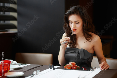 Young caucasian model with arranged hair and make-up, wearing an evening dress, serving and taste dessert in the restaurant.