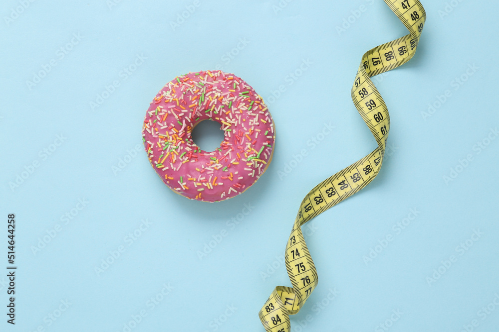 Diet concept. High calorie donut with measuring tape on blue background
