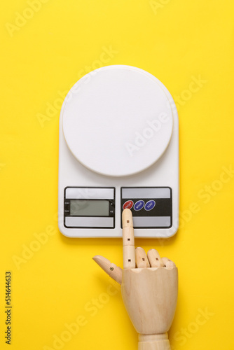 Wooden hand turns on kitchen electronic scales on a yellow background photo