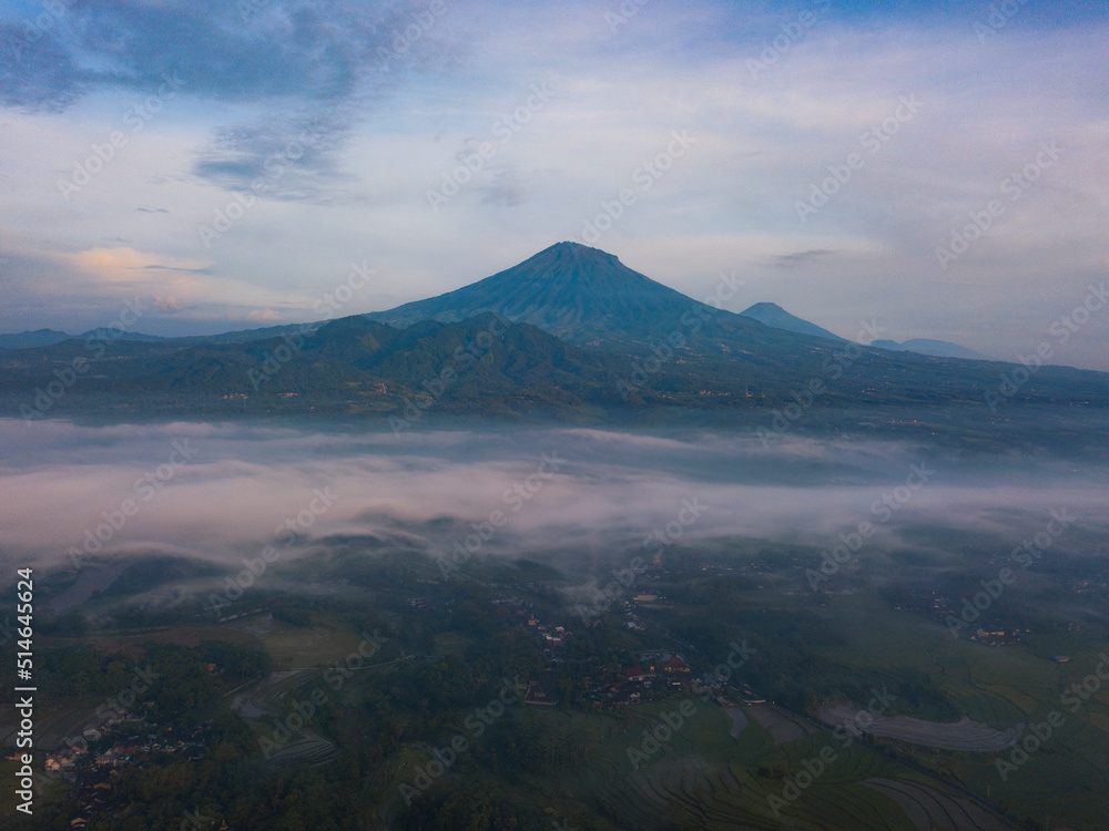 Drone photo of Mount Sumbing with sea of fog covered the land of plantation and trees in the morning. Central Java, Indonesia