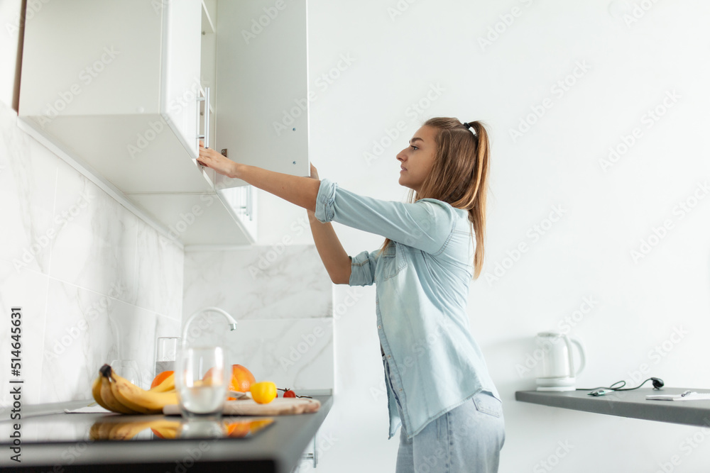 Cute young woman opens the kitchen cabinet door. Healthy food concept Cute young woman opens the kitchen cabinet door. Healthy food concept