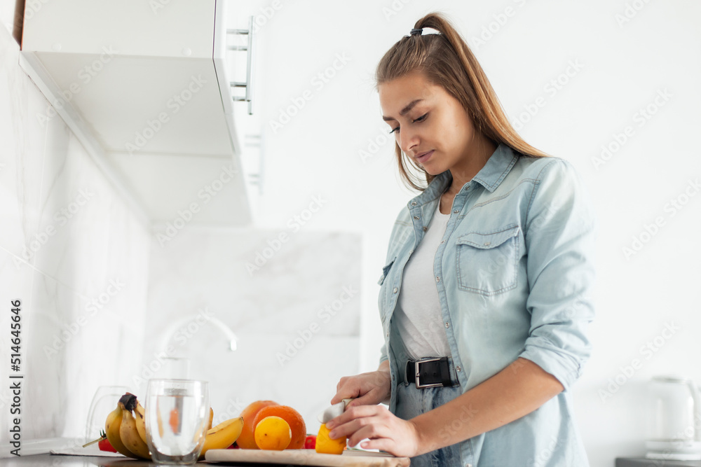 Young smiling woman cuts a lemon with a knife in the kitchen. Healthy food concept Young smiling woman cuts a lemon with a knife in the kitchen. Healthy food concept