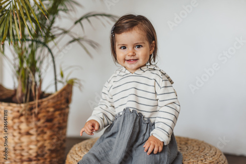Pretty one year toddler girl in grey and white stripped dress posing in eco studio. Copy space.