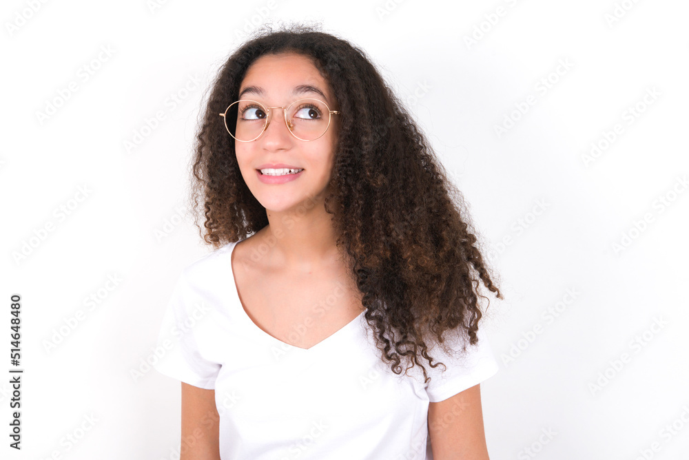 Oops! Portrait of young beautiful girl with afro hairstyle wearing white t-shirt over white wall clenches teeth and looks confusedly aside, realizes her bad mistake, Oops! Portrait of young beautiful girl with afro hairstyle wearing white t-shirt over white wall clenches teeth and looks confusedly aside, realizes her bad mistake,