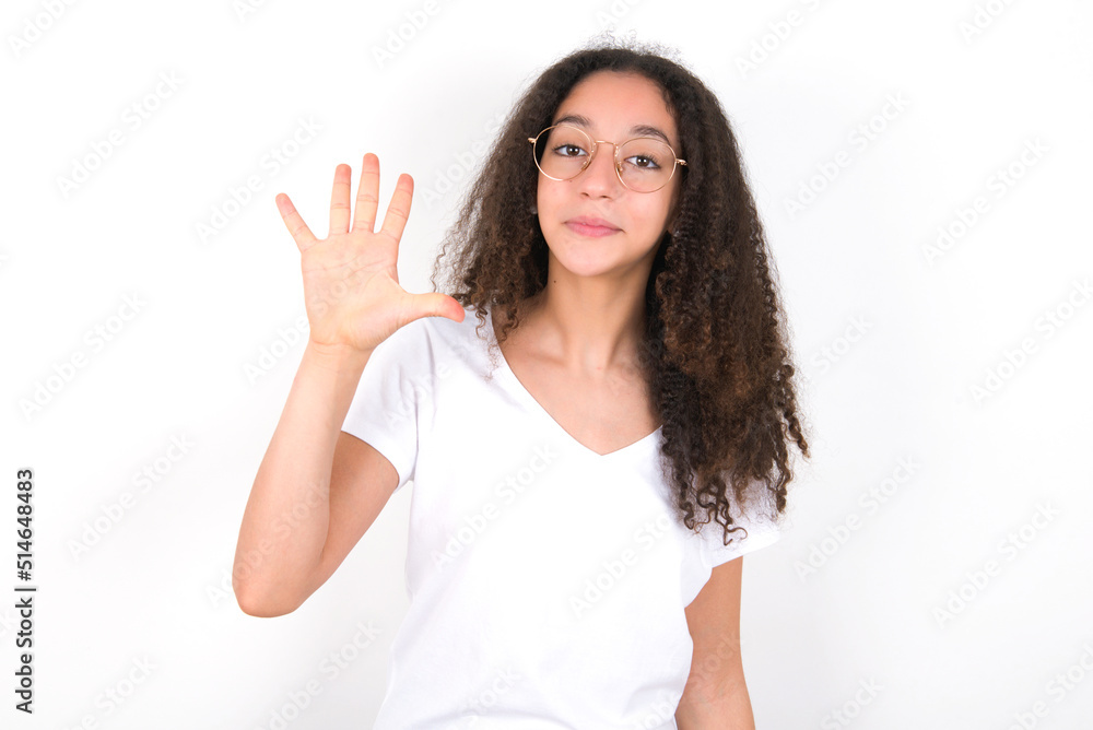 young beautiful girl with afro hairstyle wearing white t-shirt over white wall showing and pointing up with fingers number five while smiling confident and happy. young beautiful girl with afro hairstyle wearing white t-shirt over white wall showing and pointing up with fingers number five while smiling confident and happy.