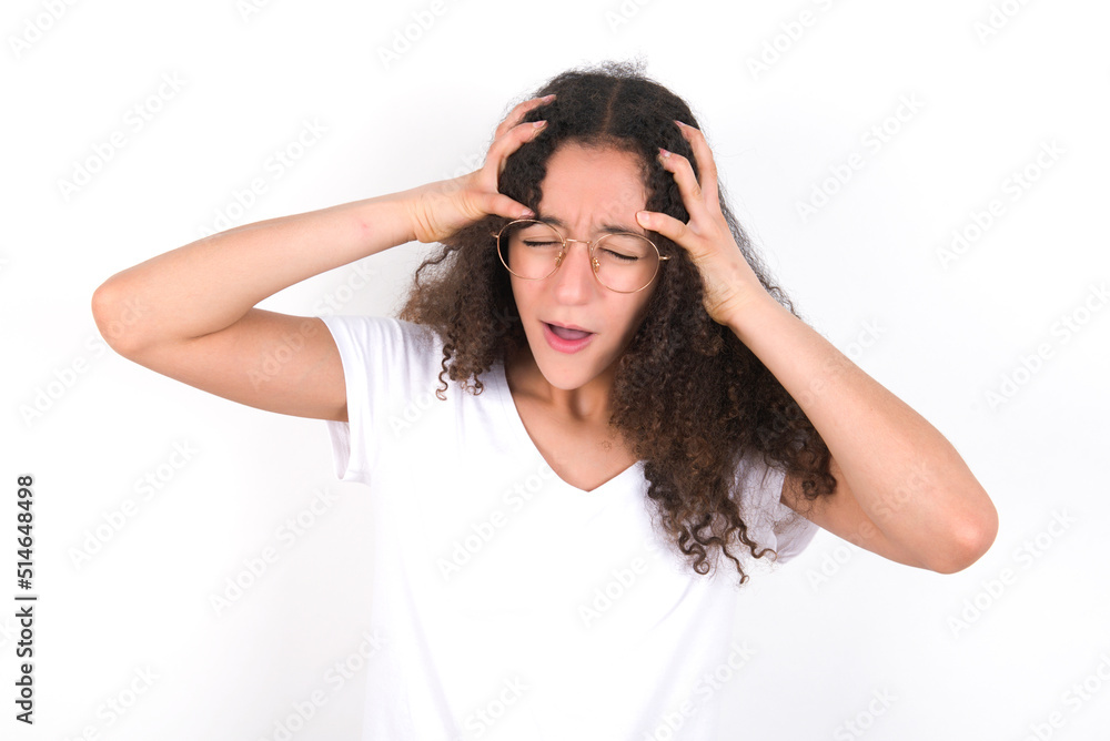 Shocked panic young beautiful girl with afro hairstyle wearing white t-shirt over white wall holding hands on head and screaming in despair and frustration. Shocked panic young beautiful girl with afro hairstyle wearing white t-shirt over white wall holding hands on head and screaming in despair and frustration.