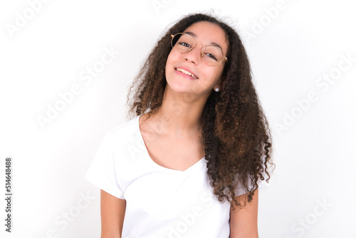 young beautiful girl with afro hairstyle wearing white t-shirt over white wall with broad smile, shows white teeth, feeling confident rejoices having day off.