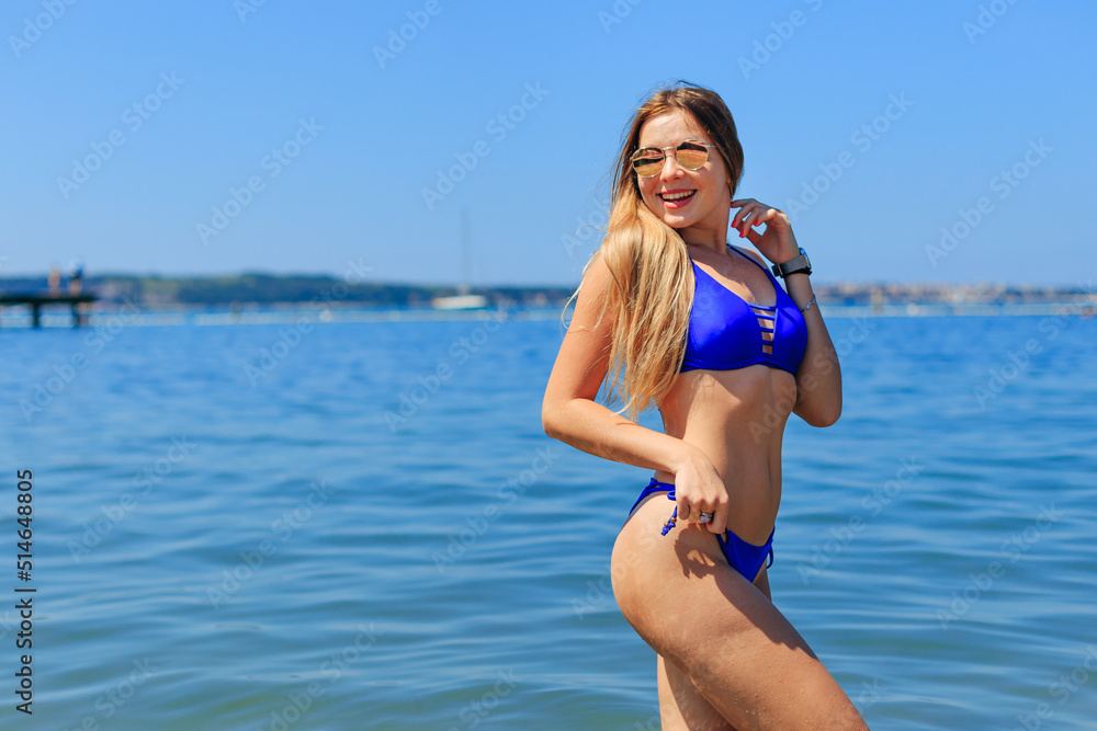 portrait of young woman in blue swimsuit and sunglasses posing in sea water