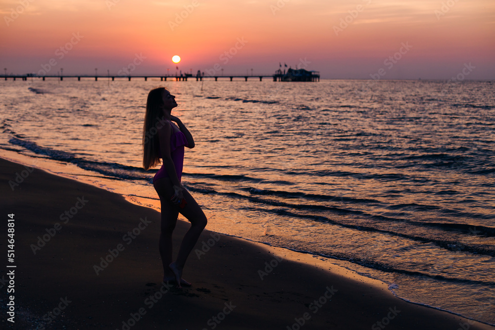 silhouette girl with long hair and fit body posing on the beach on the background of the sunset and the sea