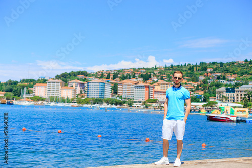 Fotografie Portoroz, Slovenia - Jul 6, 2018 young guy in sunglasses stand on the pier on the background of the sea and the city