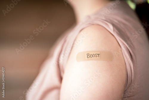 female with rolled up shirt sleeve to show the bandaid after the booster dose vaccine shot in the shoulder. To simulate covid 19 vaccine doses.